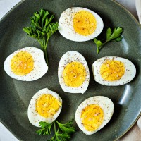 hard boiled eggs sliced in half and sprinkled with salt and pepper on a green plate with parsley garnish.