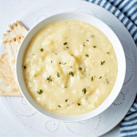 a bowl of potato soup on a white plate with crackers to the side and fresh thyme leaves sprinkled on top.