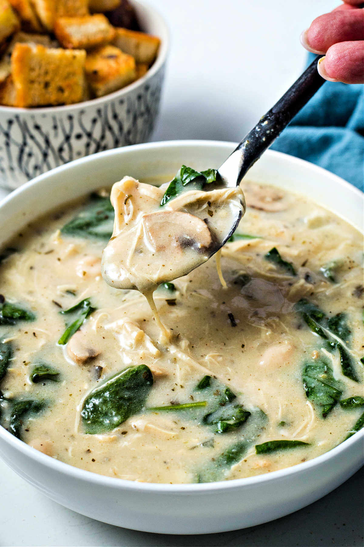 a spoon lifting out a bite of chicken florentine soup from a bowl,