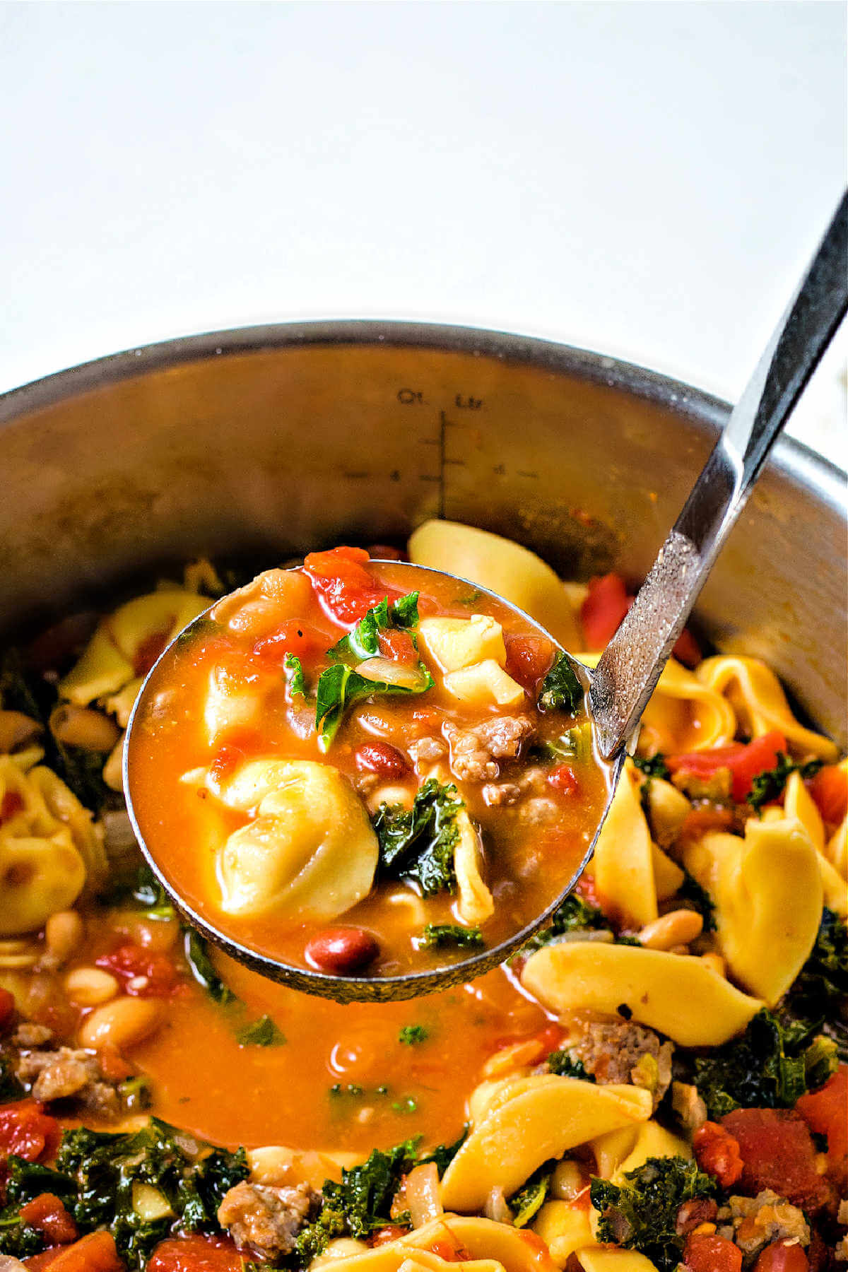 a ladle lifting out of a pot of sausage tortellini soup,