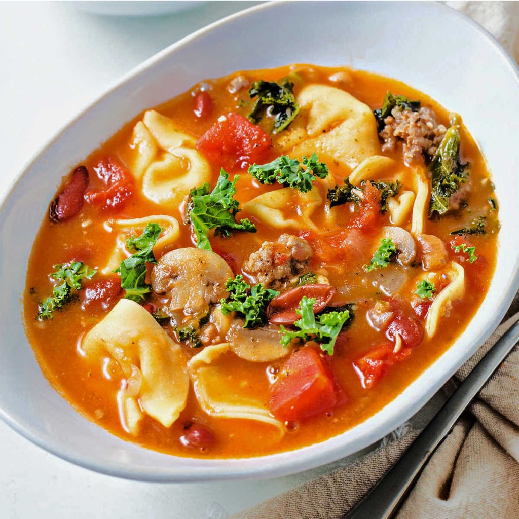 sausage tortellini soup with kale in a white bowl on a table.