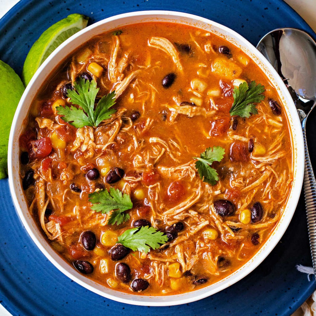 a bowl of slow cooker chicken enchilada soup sitting on a blue plate with lime wedges.