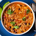 a bowl of slow cooker chicken enchilada soup sitting on a blue plate with lime wedges.