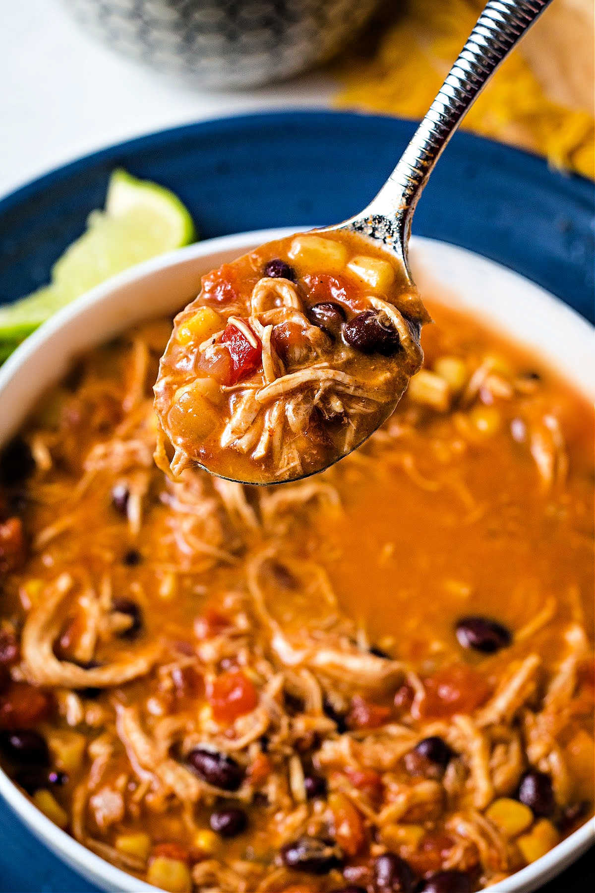 close up of a spoon lifting up out of a bowl of slow cooker chicken enchilada soup.