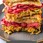 a corned beef reuben with coleslaw sandwich cut in half and stacked on a plate with a pick through the center.