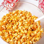 cheddar cheese popcorn in a clear bowl with a scoop.