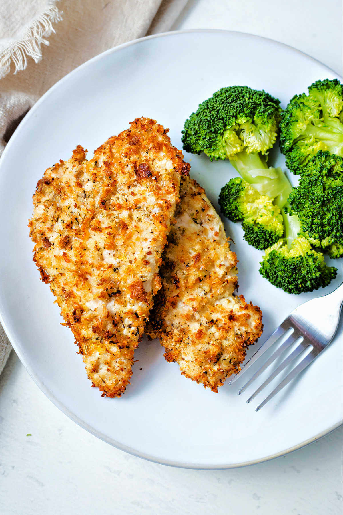 two air fryer chicken cutlets on a white plate with a side of broccoli.
