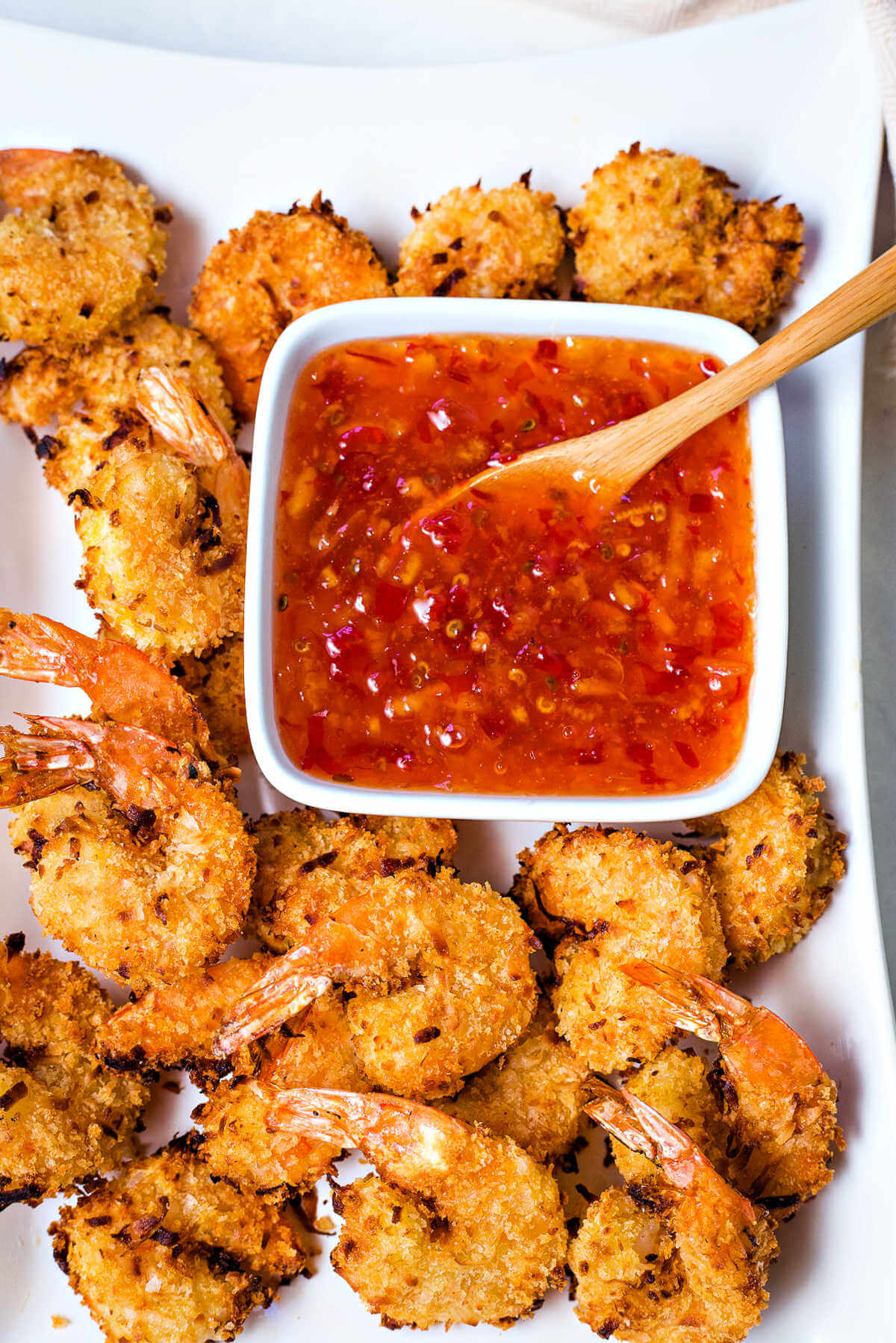 air fryer coconut shrimp on a white platter with a bowl of dipping sauce.