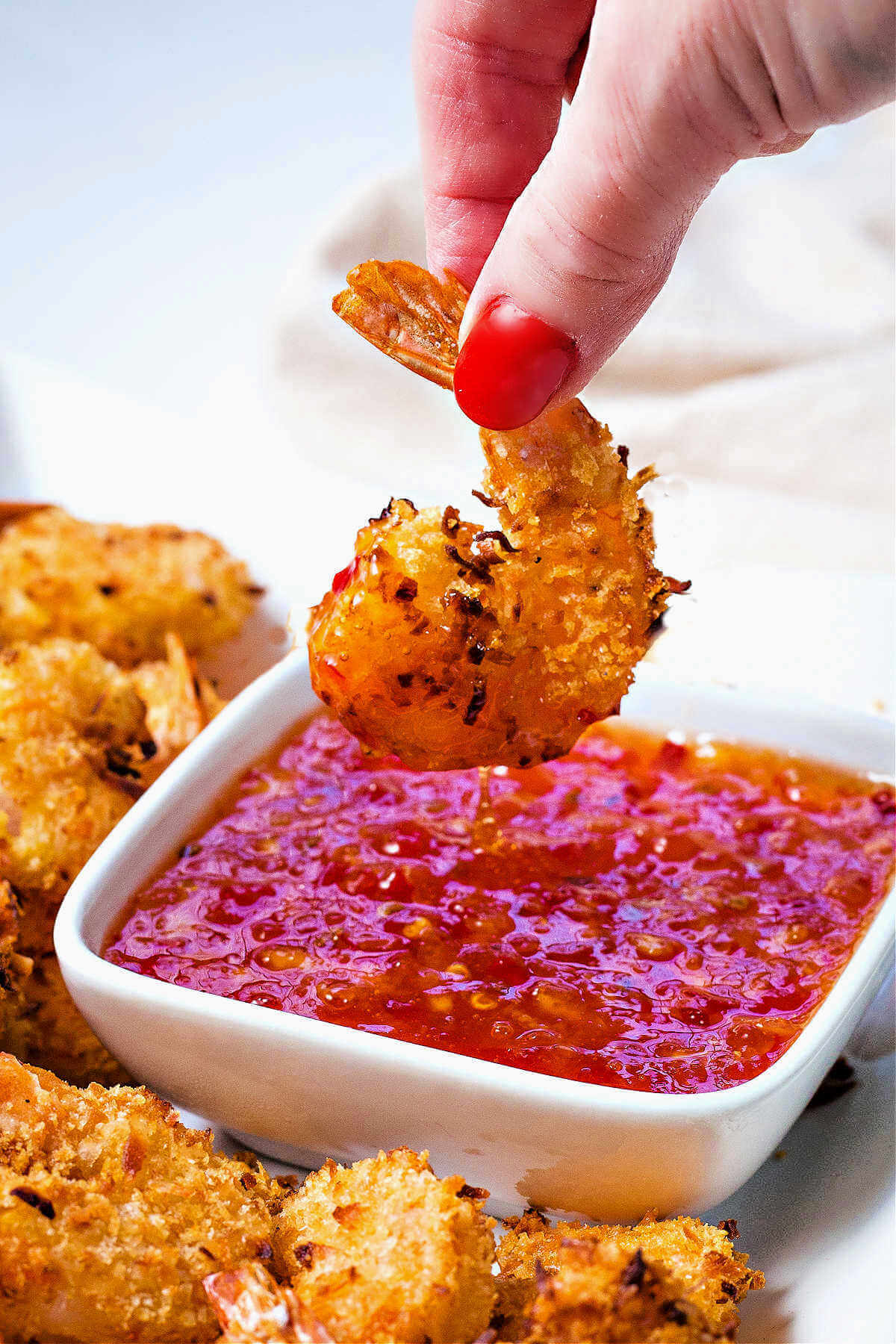 a piece of air fryer coconut shrimp being dipped into a bowl of sauce.