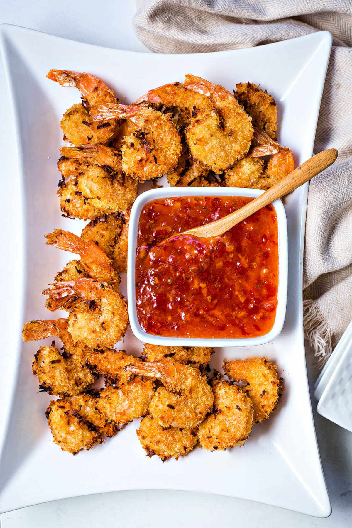 air fryer coconut shrimp on a white platter with a bowl of dipping sauce.