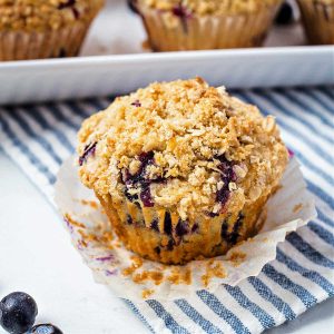 a blueberry oatmeal muffin sitting in a paper liner on a blue striped napkin.