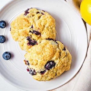 two blueberry scones on a white plate with blueberries scattered on the side.