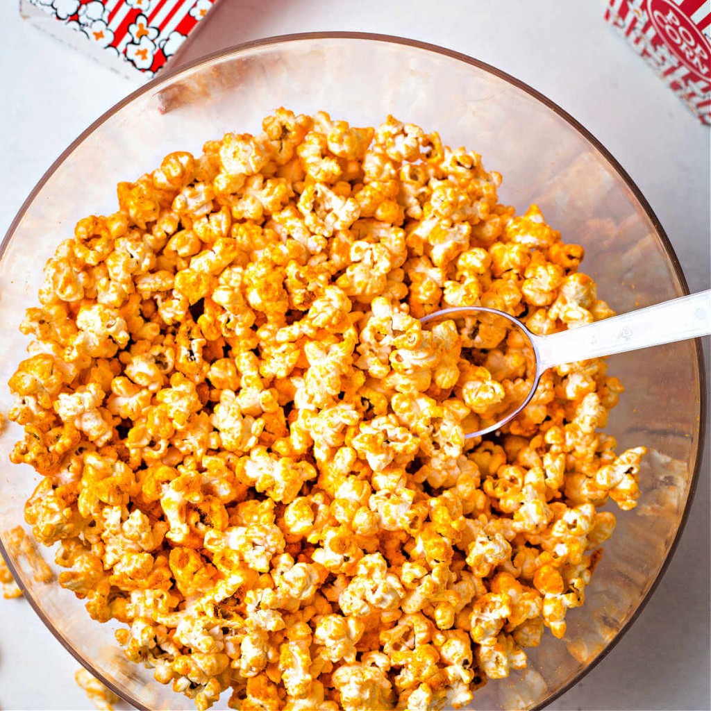 cheddar cheese popcorn in a clear bowl with a scoop.