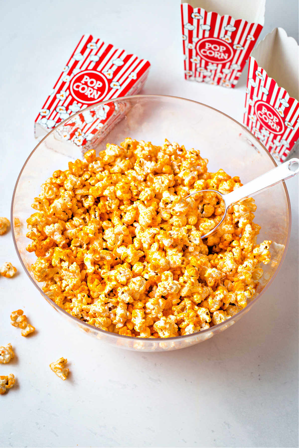 cheddar cheese popcorn in a clear bowl with a scoop and red and white popcorn boxes in the background.