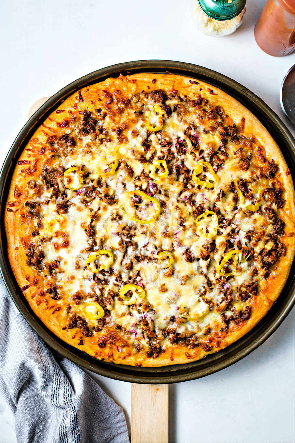 baked cheeseburger pizza in a pizza pan on top of a pizza wheel.