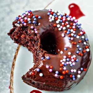a chocolate glazed donut with a bite taken out of perched on a plate.