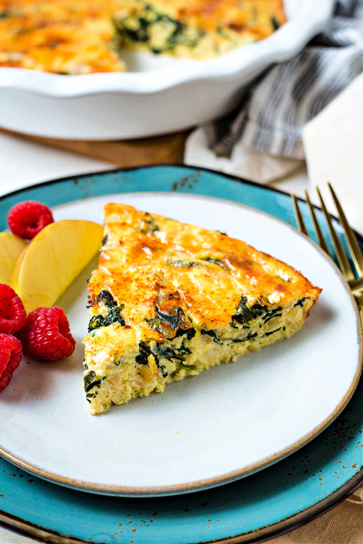 a slice of crustless spinach quiche on a plate with fresh fruti.