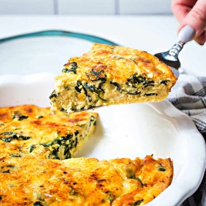 a pie server lifting out a slice of crustless spinach quiche from a baked quiche.