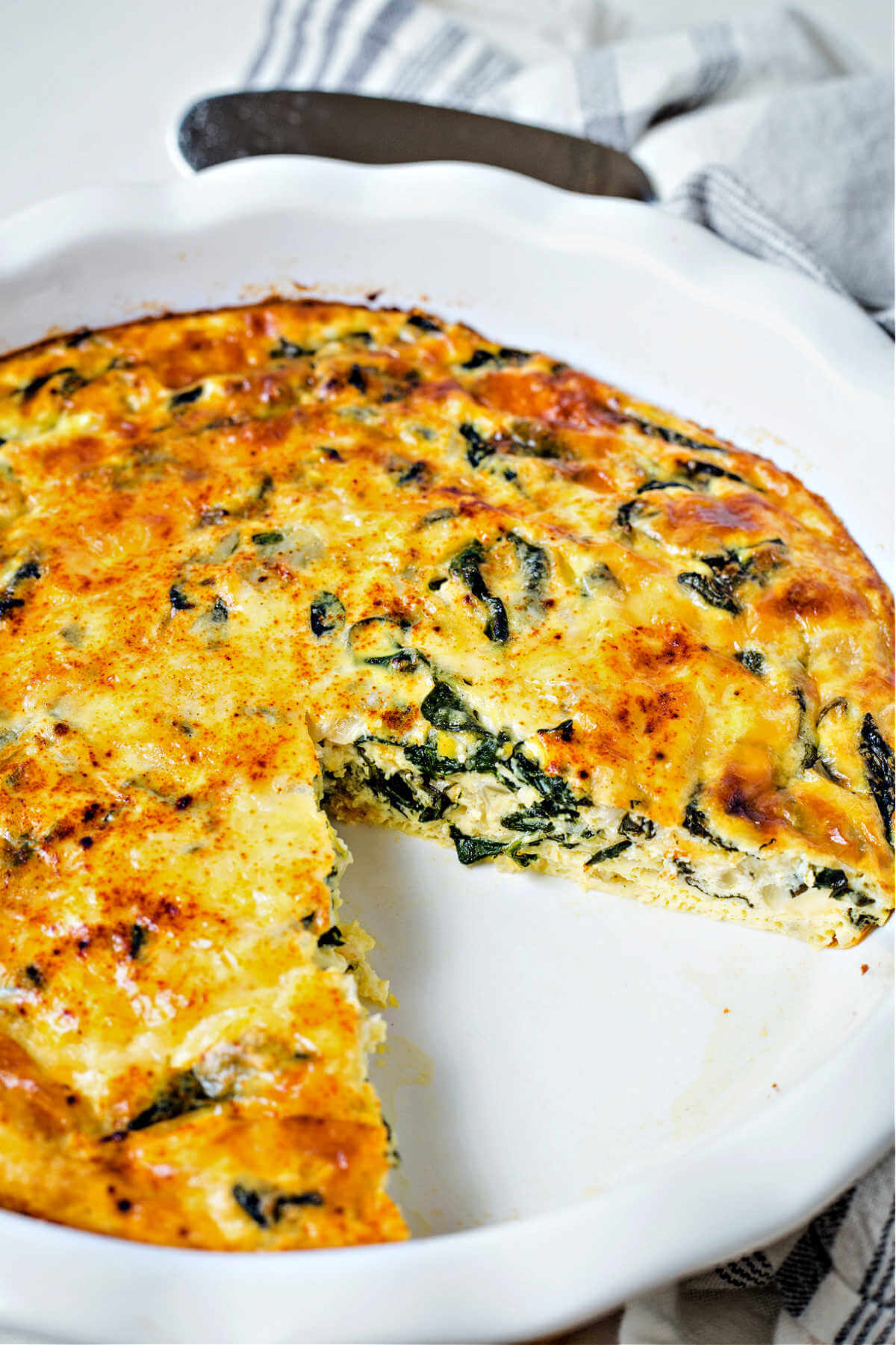 crustless spinach quiche with a slice missing sitting on a table.