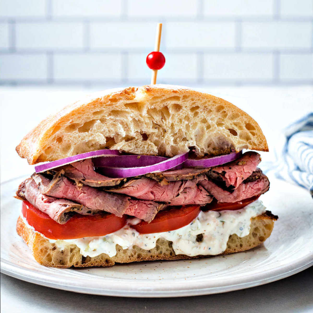 a steak sandwich on a ciabatta bun with tomatoes and red onions.