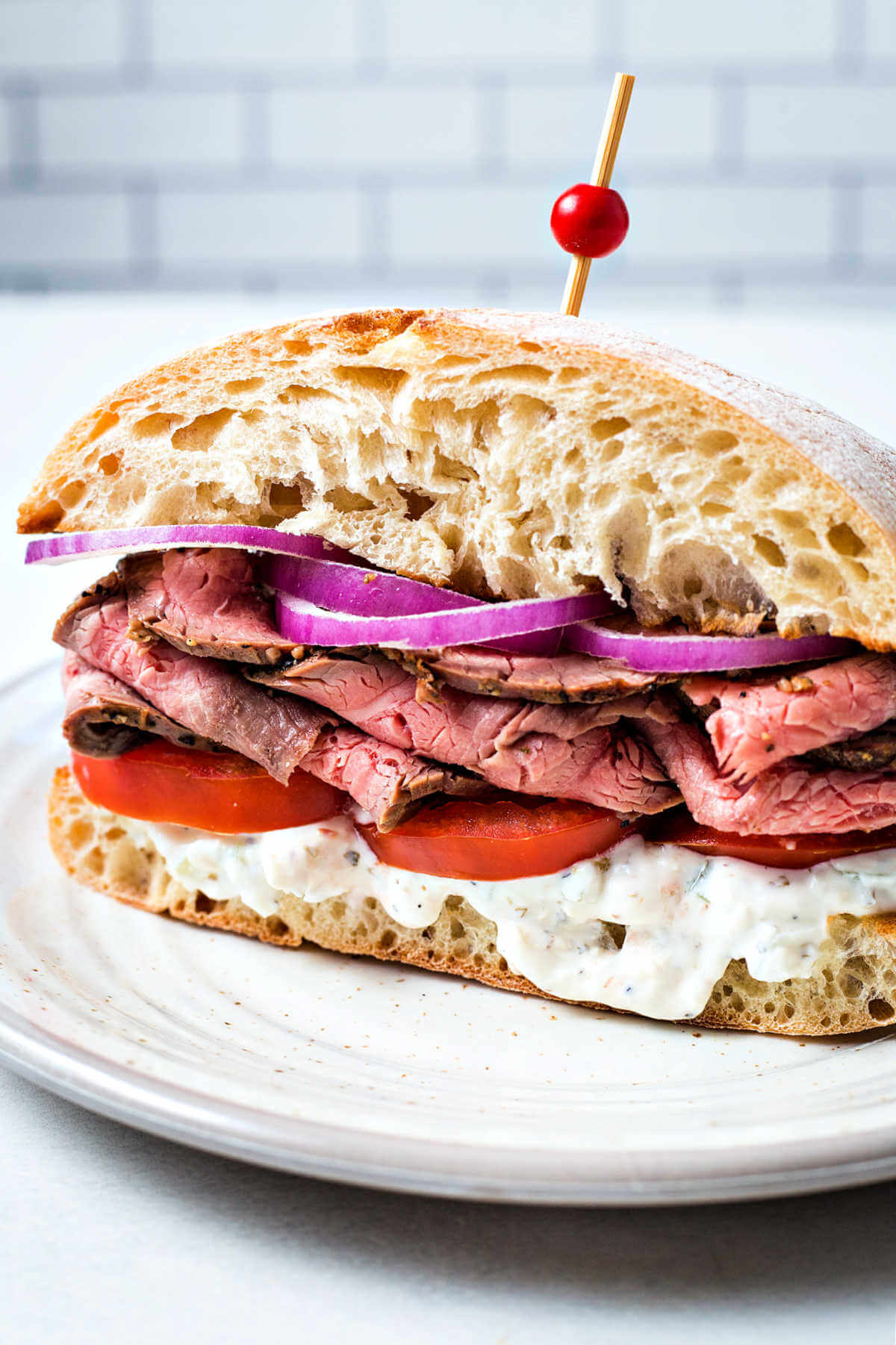 a steak sandwich on a ciabatta bun with tomatoes and red onions.