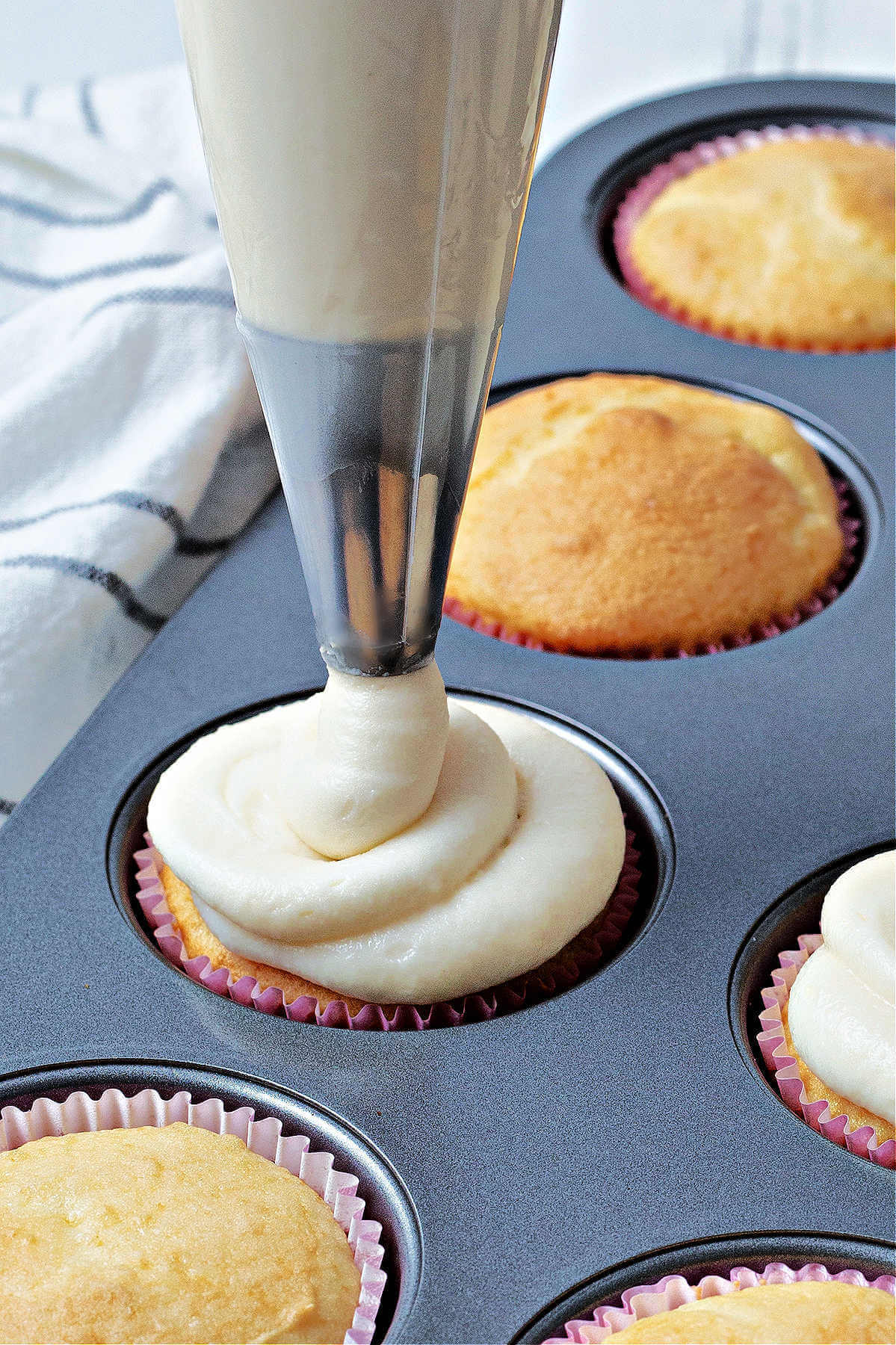close up image of piping sour cream frosting onto a vanilla cupcake.
