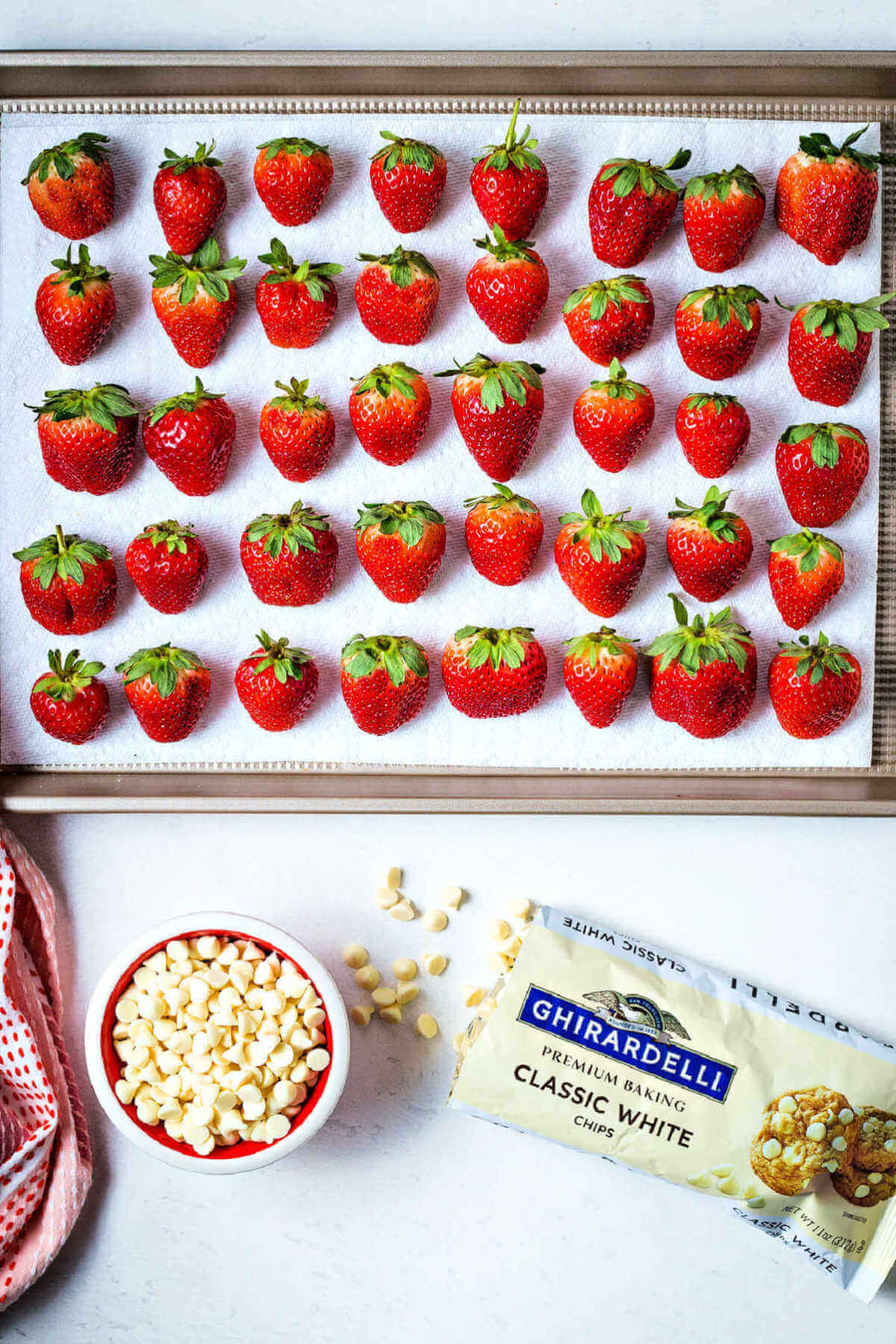 fresh strawberries drying on a paper towel lined baking sheet with a bag of white chocolate chips on the counter.