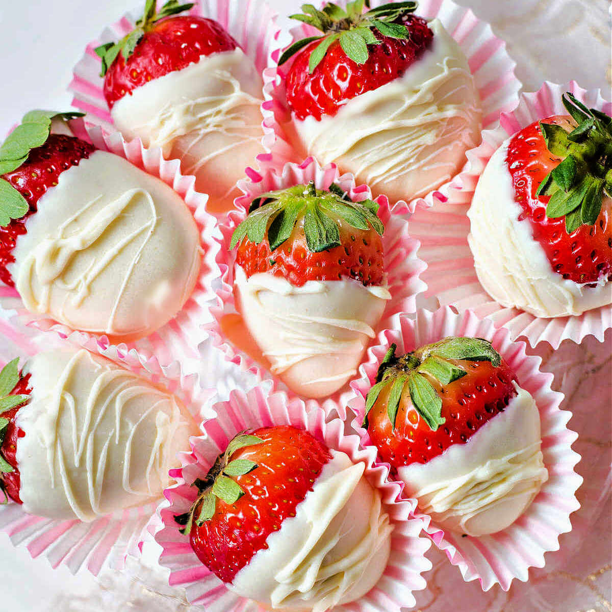 white chocolate covered strawberries in paper wrappers on a glass pedestal plate.