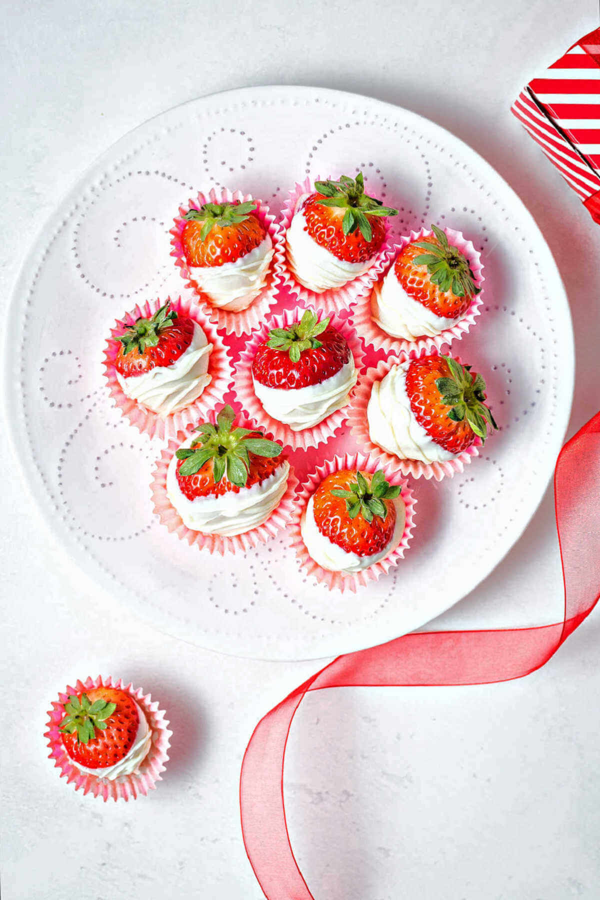 a plate of white chocolate dipped strawberries with red ribbon in the background.