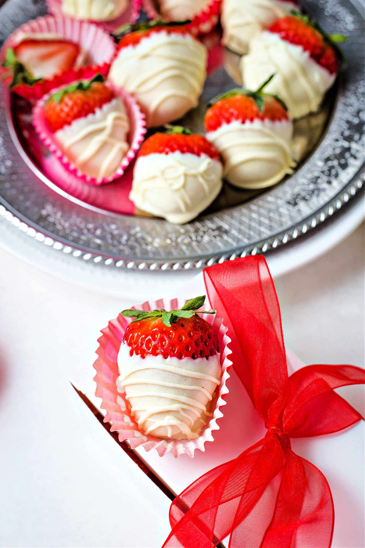 a gift box tied with a red ribbon with a white chocolate dipped strawberry sitting on top.