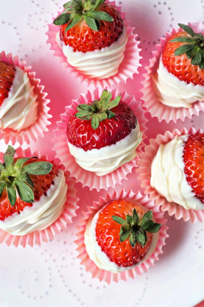 white chocolate covered strawberries in paper wrappers on a glass pedestal plate.