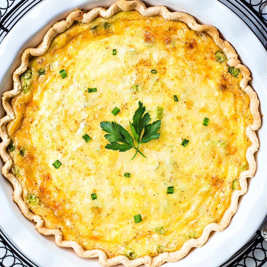 top down view of a whole baked quiche lorraine sitting on. a decorative charger on a table.