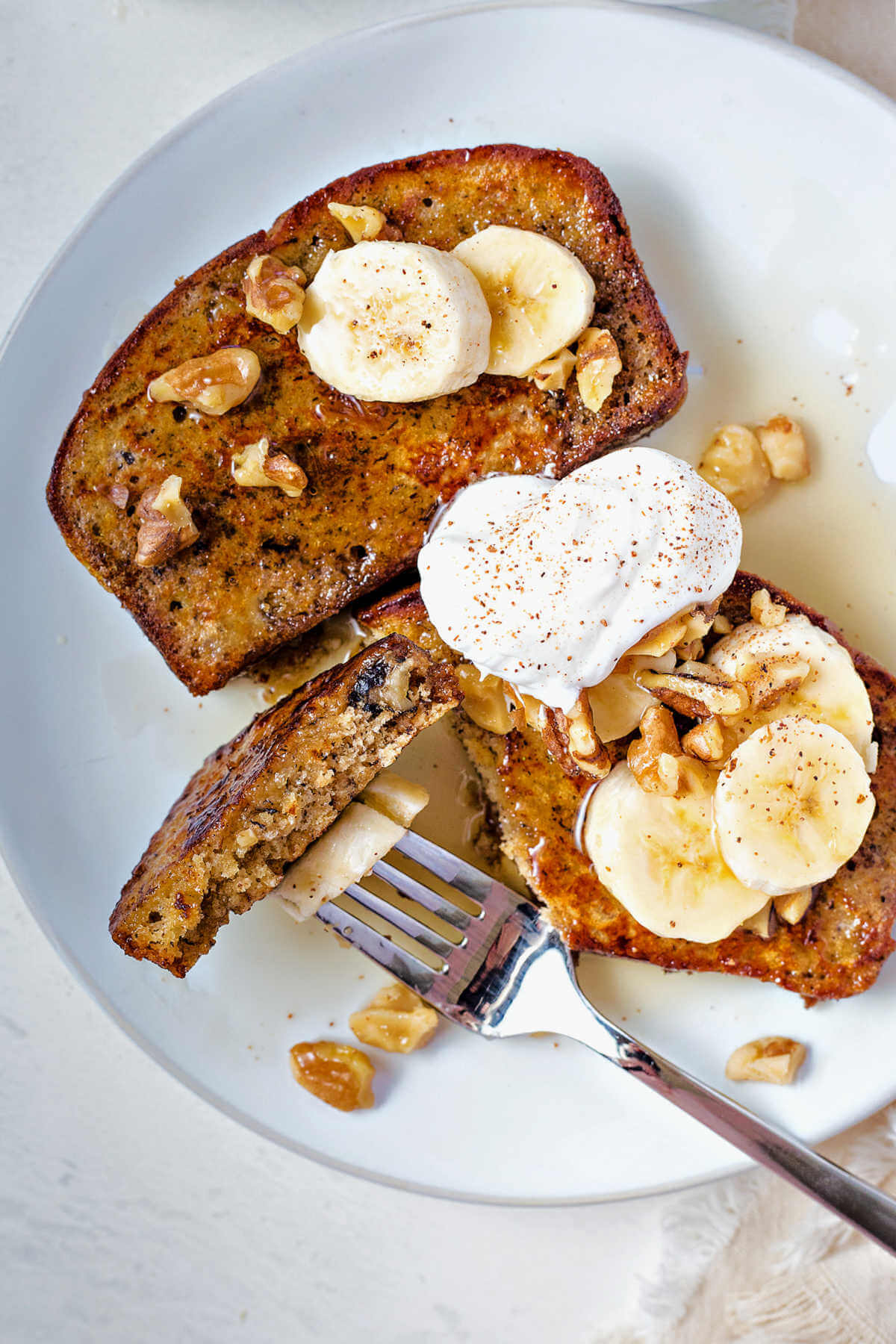 two slices of banana bread french toast on a plate with a bite speared on a fork.
