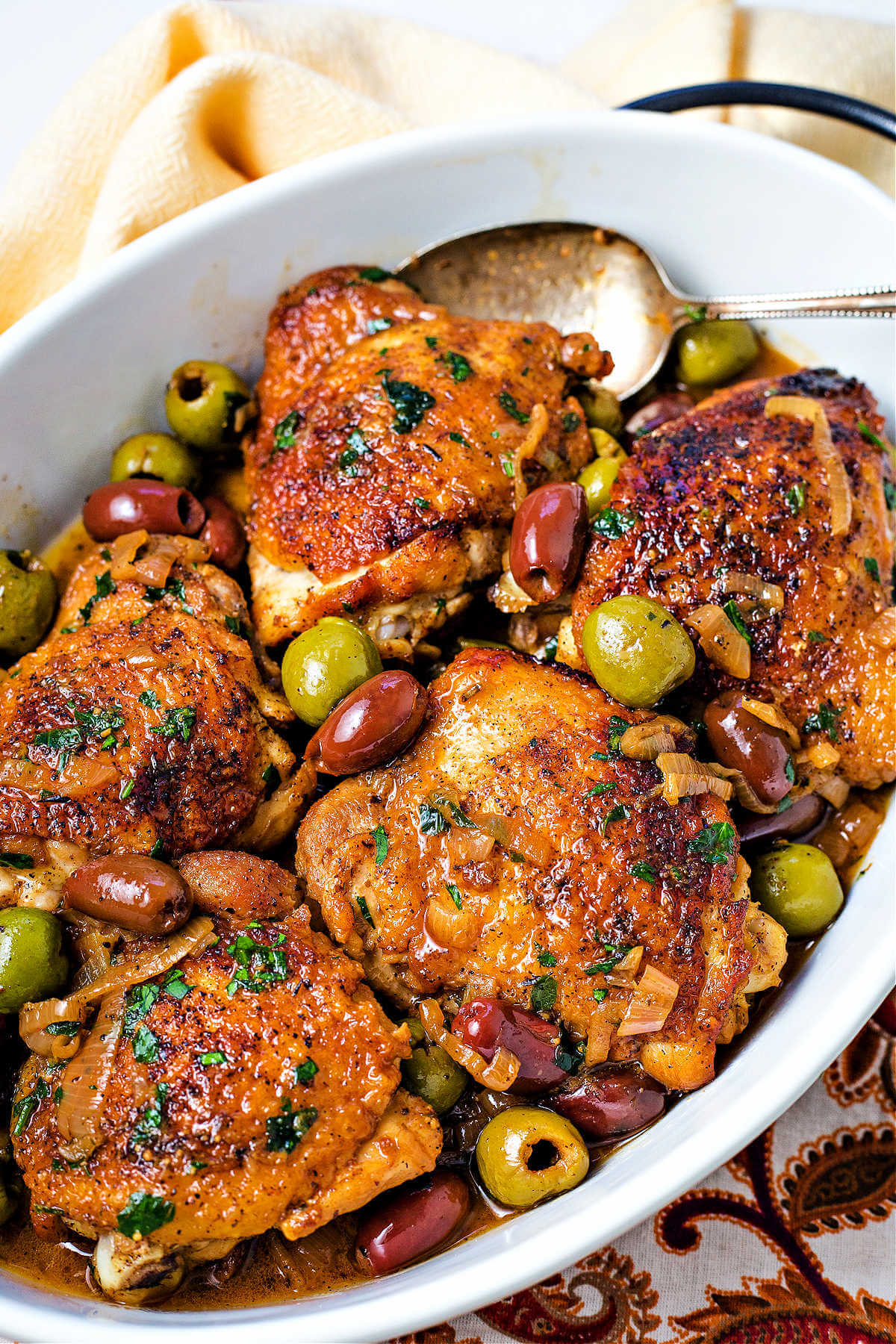browned chicken thighs with olives in a white oval serving dish.
