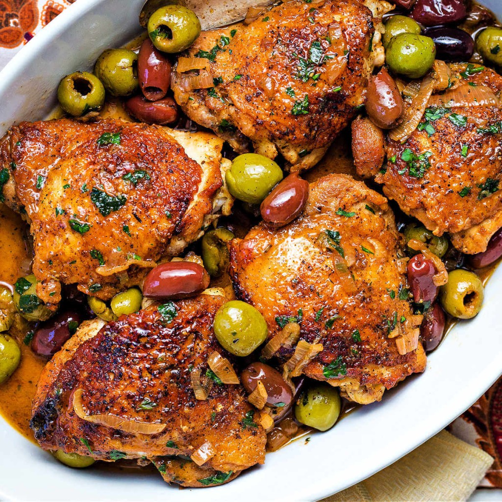 browned chicken thighs with olives in a white oval serving dish.