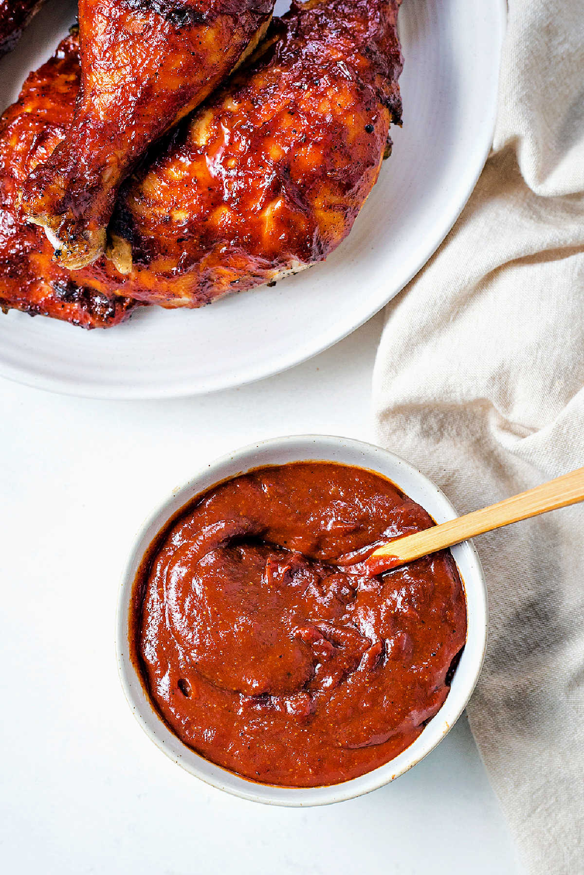 barbecue sauce in a bowl on a table with a platter of chicken in the background.