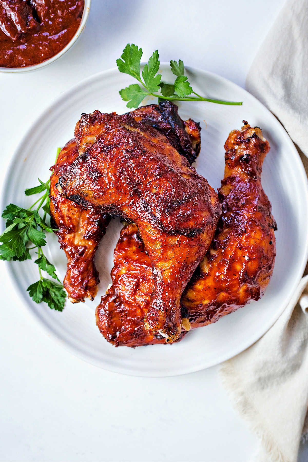 oven barbecue chicken leg quarters on a plate garnished with parsley with a bowl of barbecue sauce in the background.