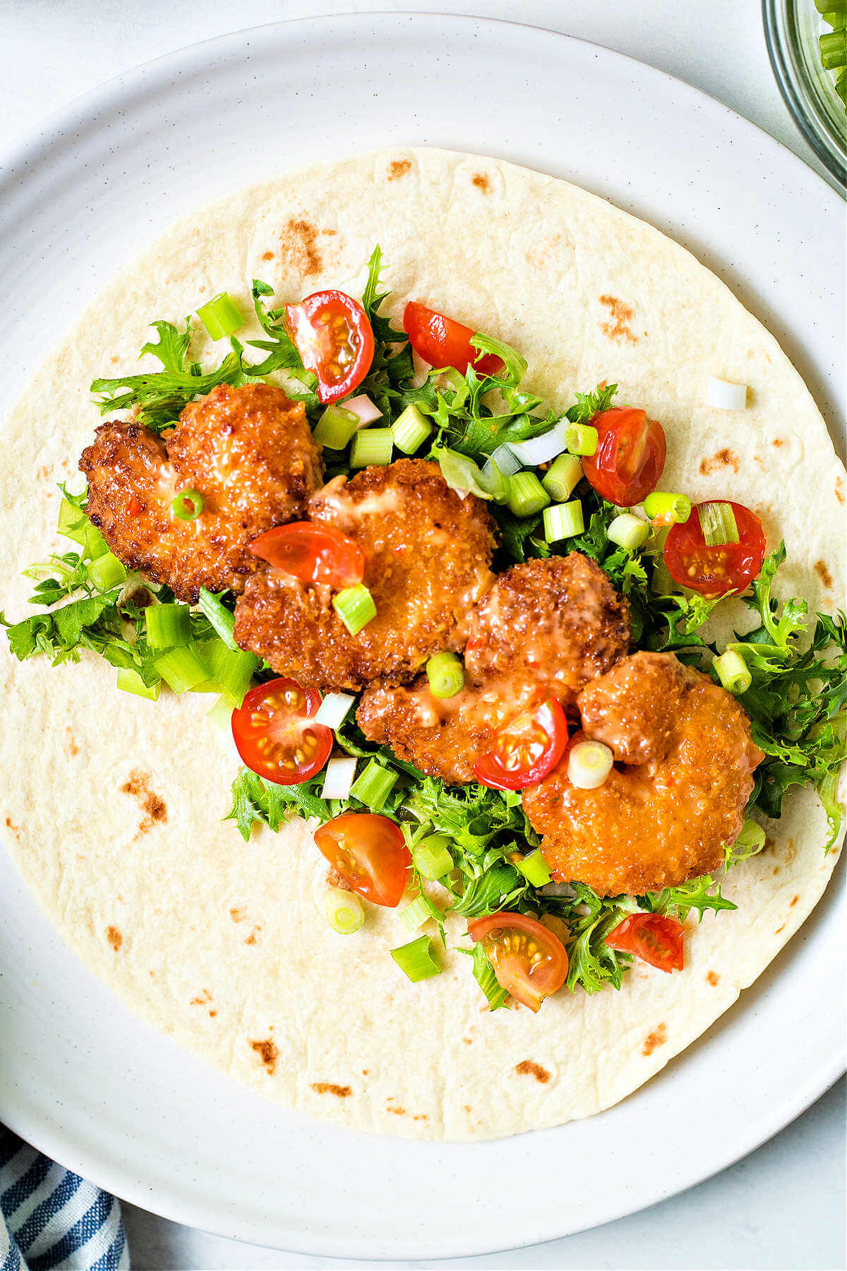 bang bang shrimp layered on a soft tortilla with lettuce, tomatoes, onions, and bang bang saucee.