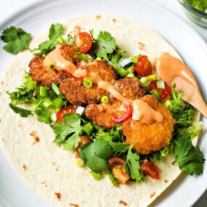 a bang bang shrimp taco on a white plate with a bowl of bang bang sauce to the side.