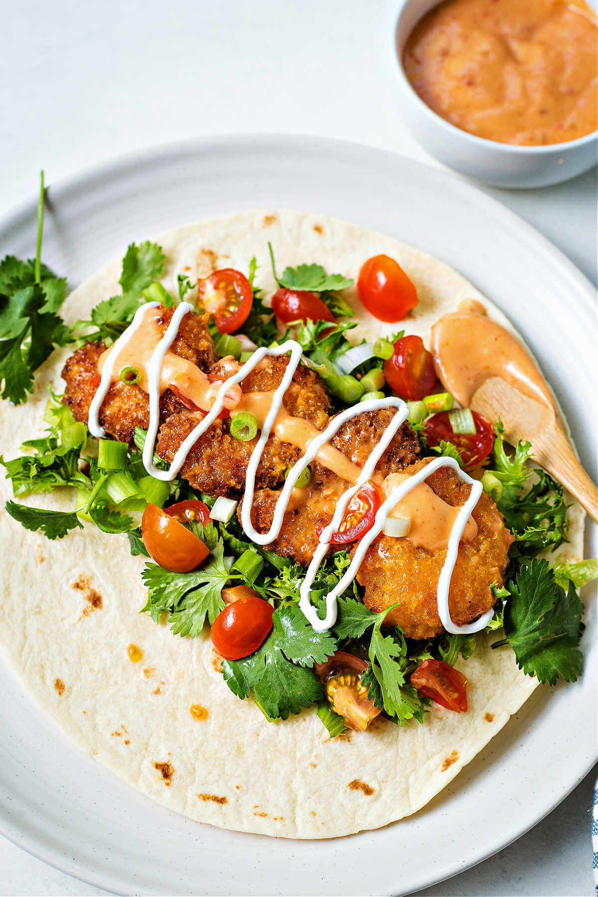 a bang bang shrimp taco on a white plate with a bowl of bang bang sauce to the side.