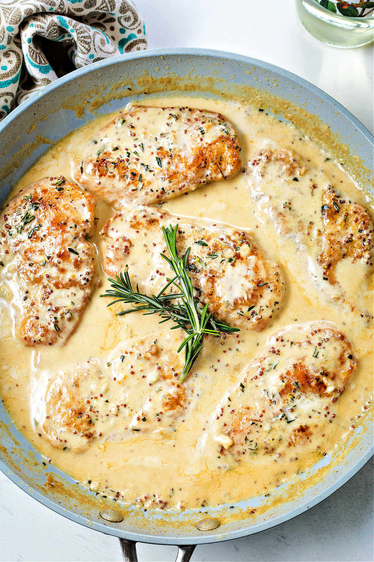 chicken dijon simmering in sauce in a skillet with a sprig of rosemary on top.