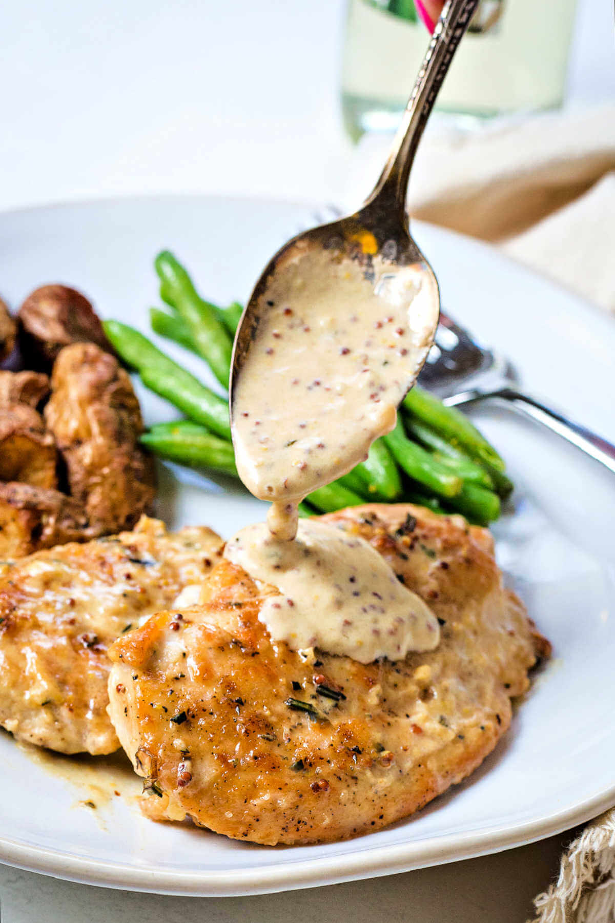 a spoon ladeling mustard sauce over chicken cutlets on a plate.
