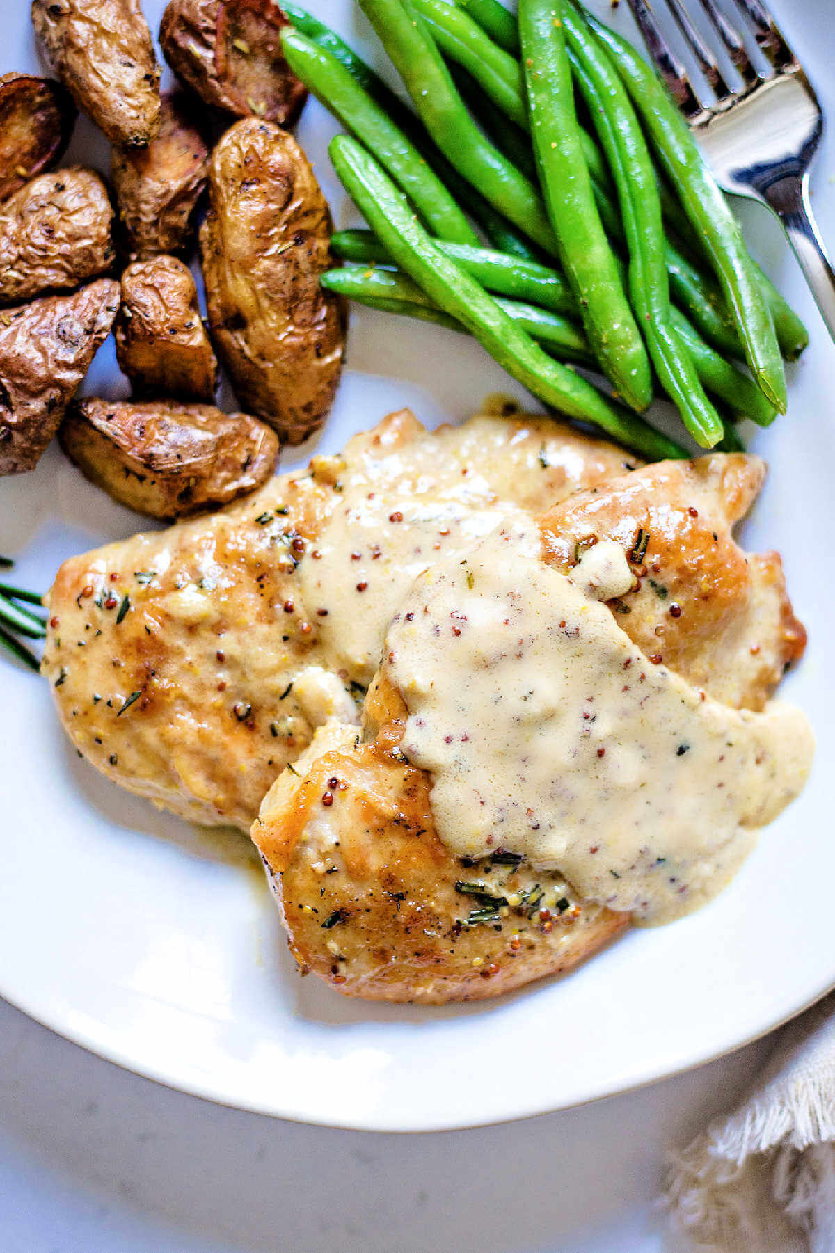 chicken dijon with sauce ladled on top on a dinner plate with a fork.