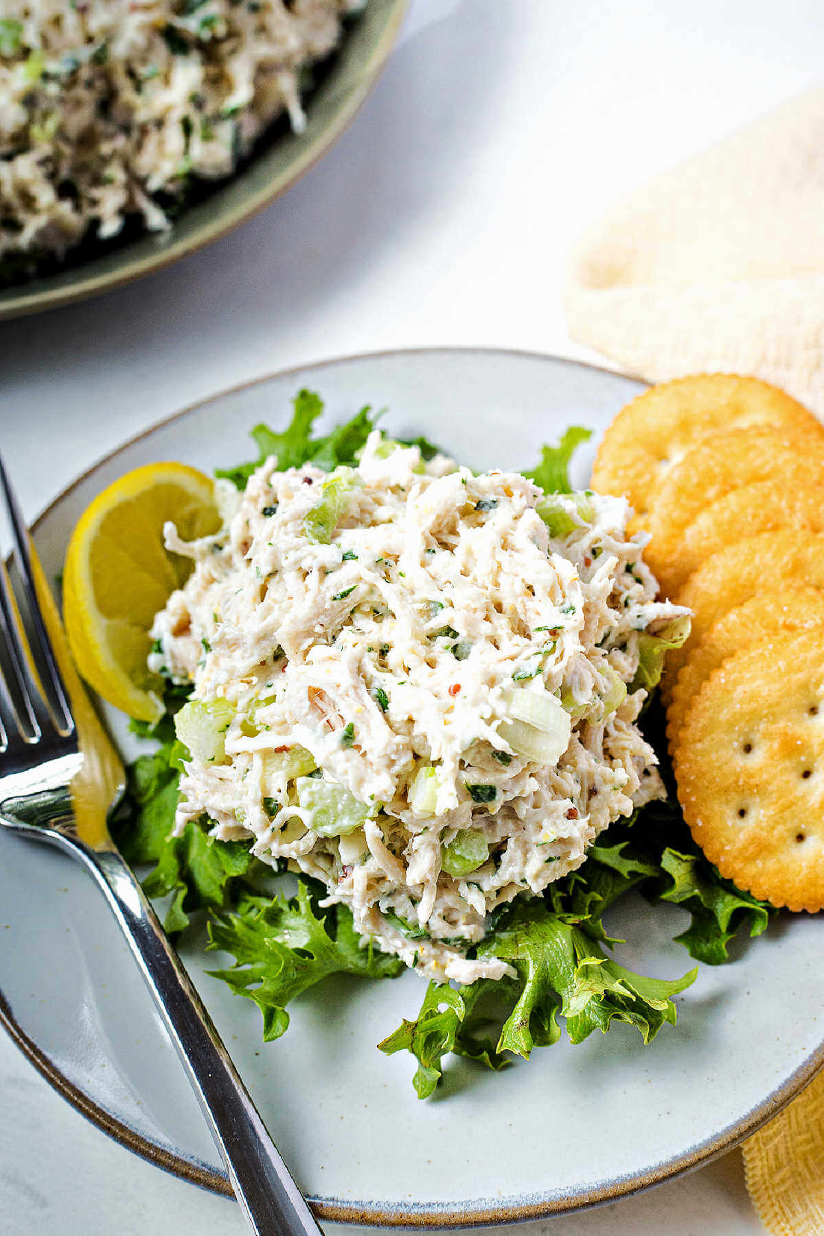 a scoop of chicken salad on a bed of lettuce with Ritz crackers and a lemon wedge on the side.