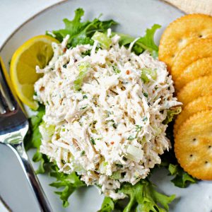 a scoop of chicken salad on a bed of lettuce with Ritz crackers and a lemon wedge on the side.