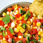 corn salsa in a serving bowl surrounded by tortilla chips.