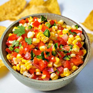 corn salsa in a serving bowl surrounded by tortilla chips.