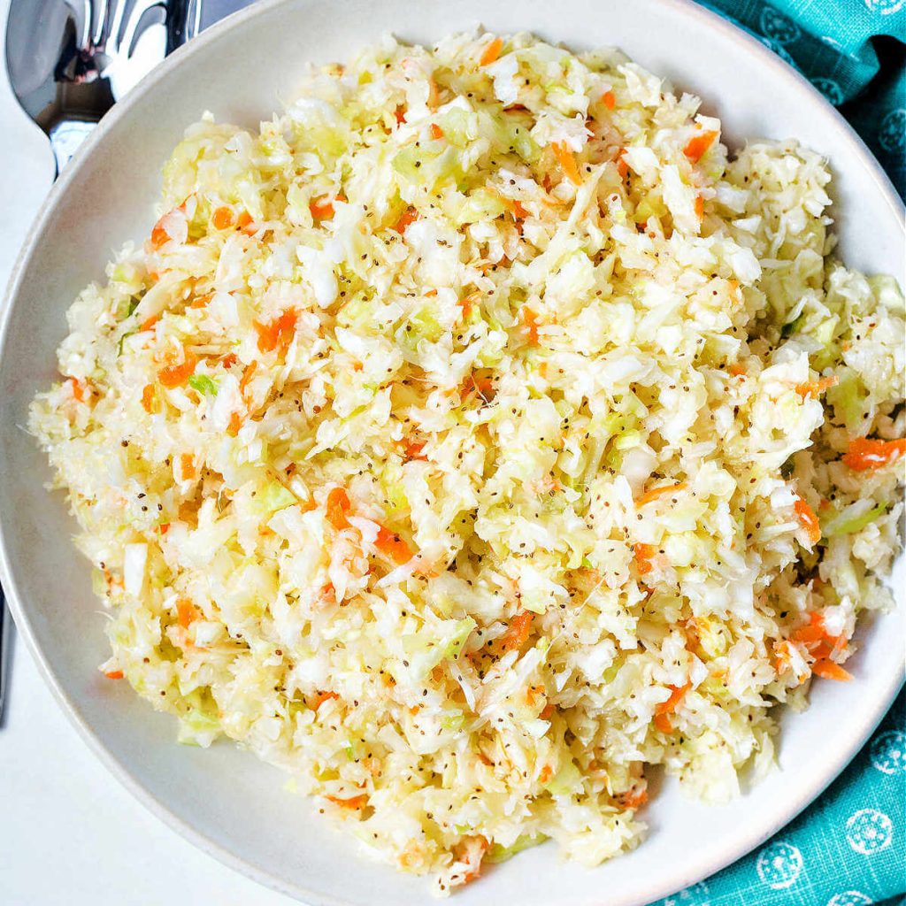 no mayo coleslaw in a bowl on a table with a napkin and slotted spoon.