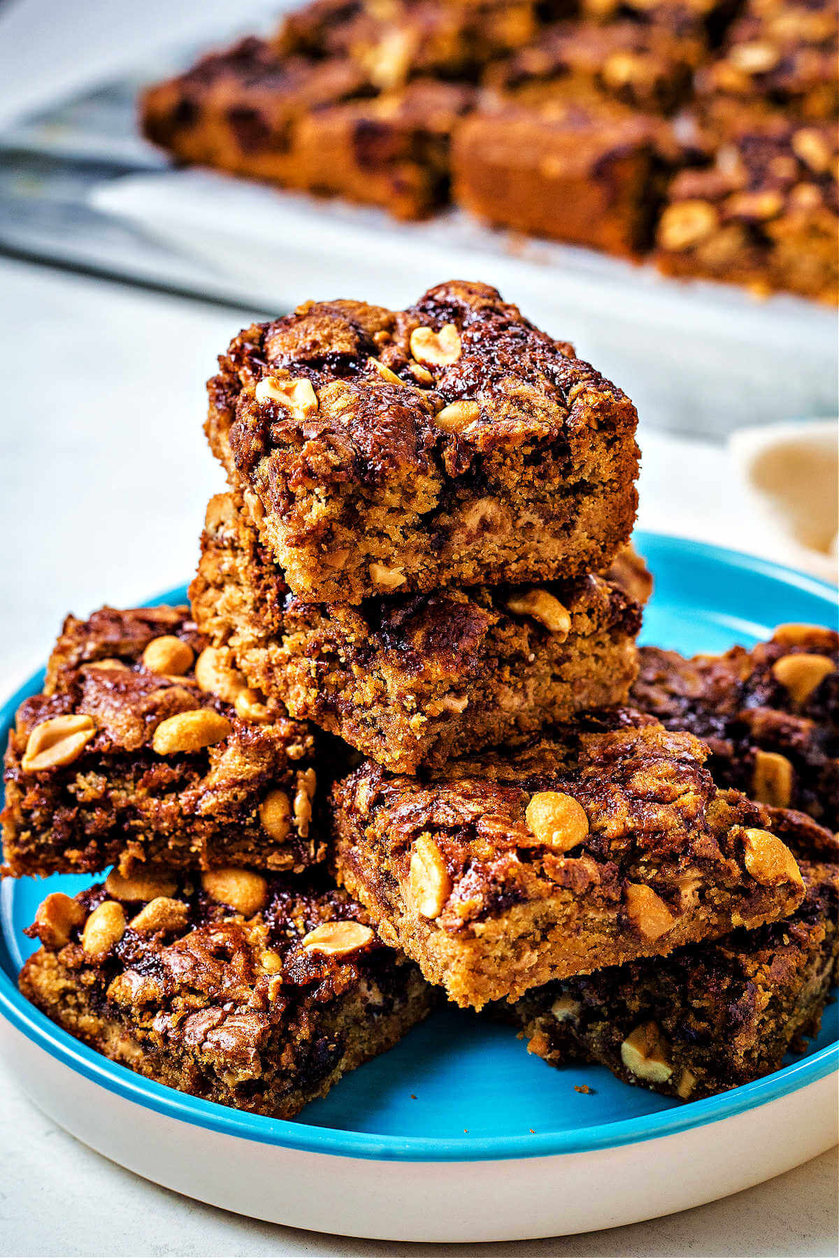 peanut butter brownies stacked on top of each other on a blue plate on a table with more brownies in the background.