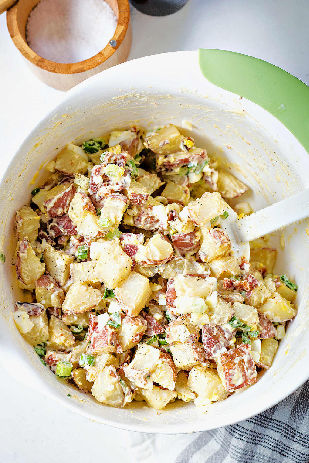 stirring mayonnaise into a bowl of red potato salad with a rubber spatula.